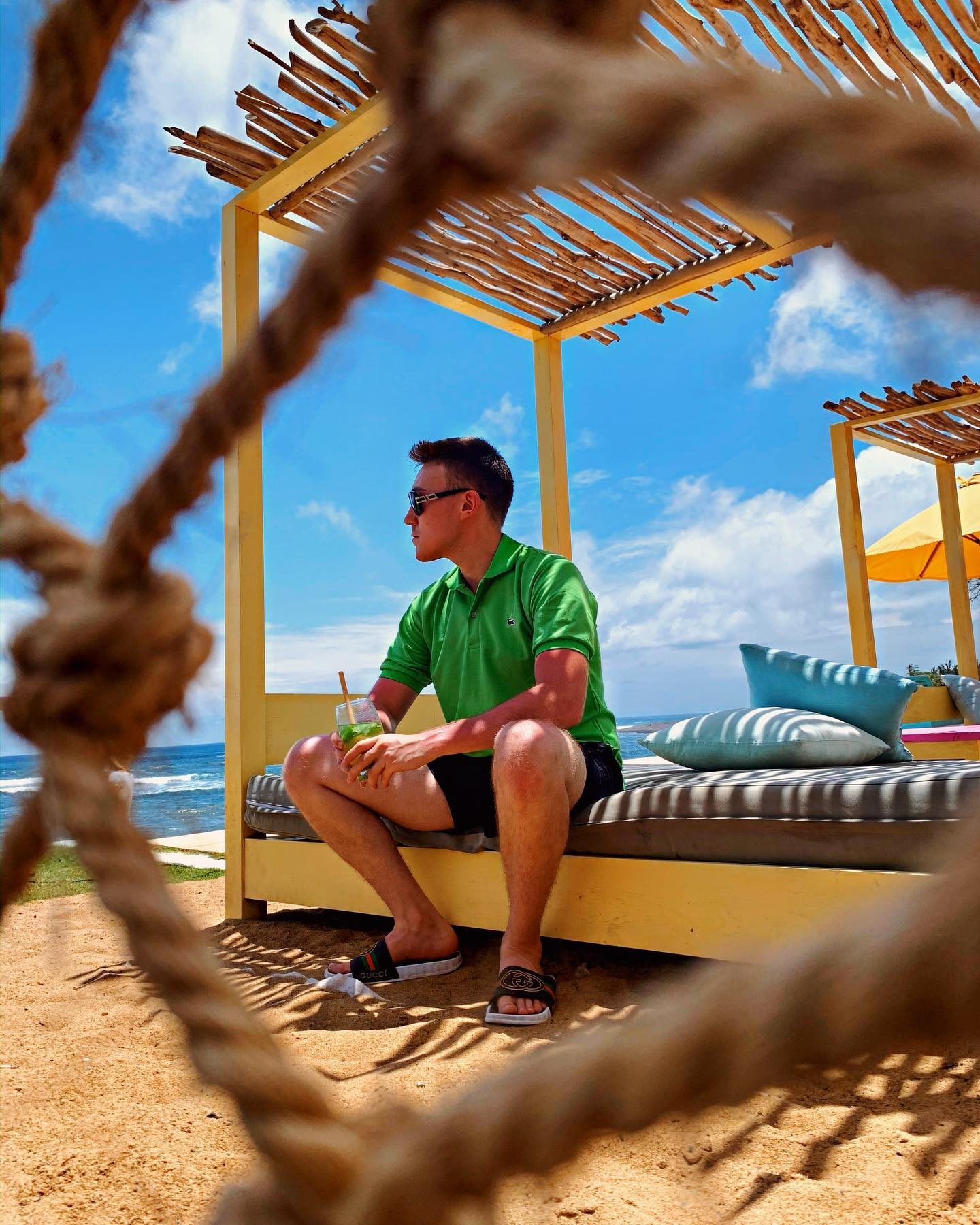 Arthur sitting in a beach cabana, seen through a rope frame