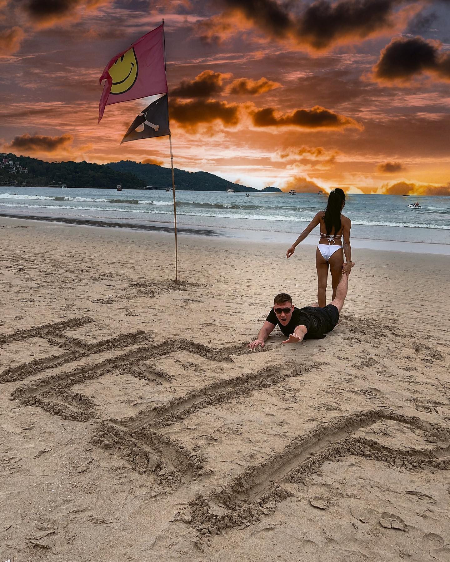 Dramatic sunset at a beach with flags and sand writing
