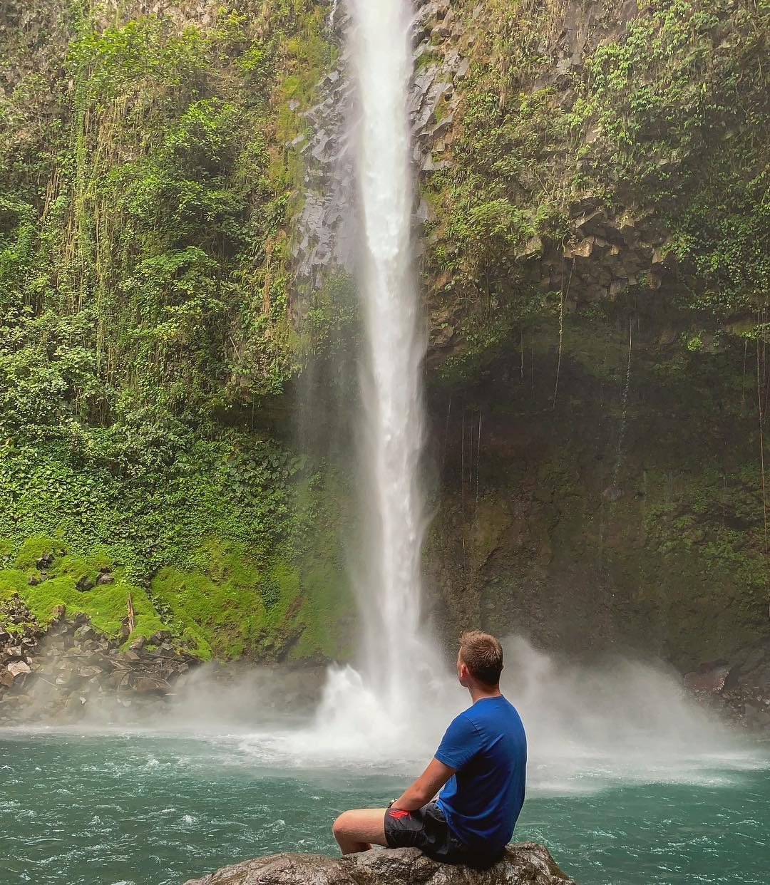 Arthur sitting on a rock in front of a jungle waterfall